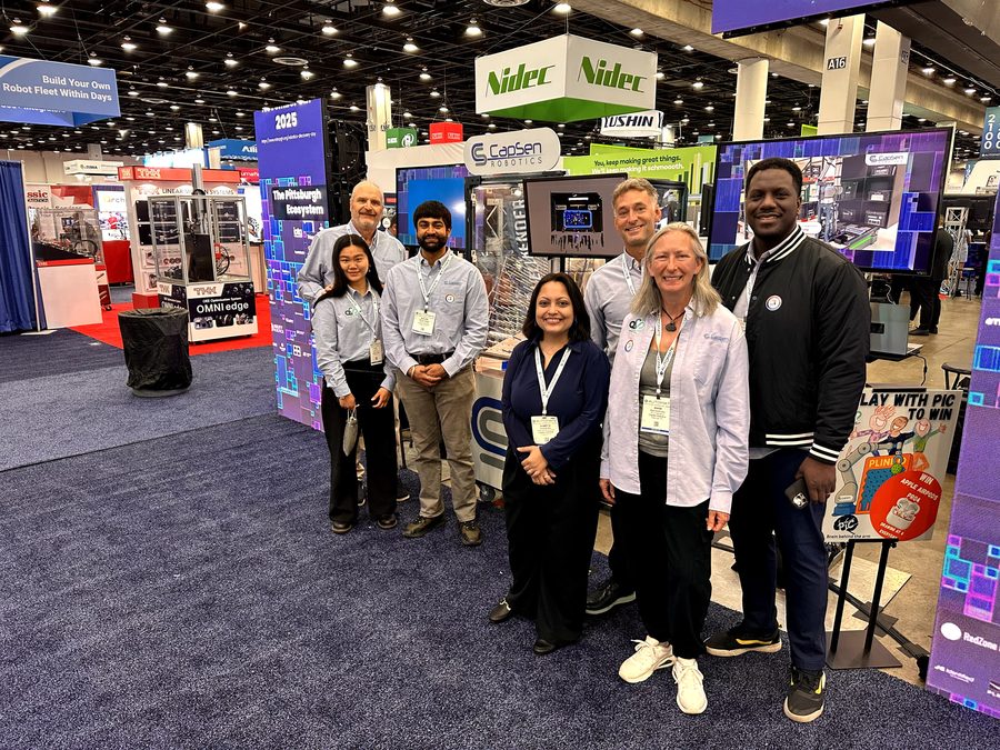 Another group photo with the booth screens and robotics demonstration.